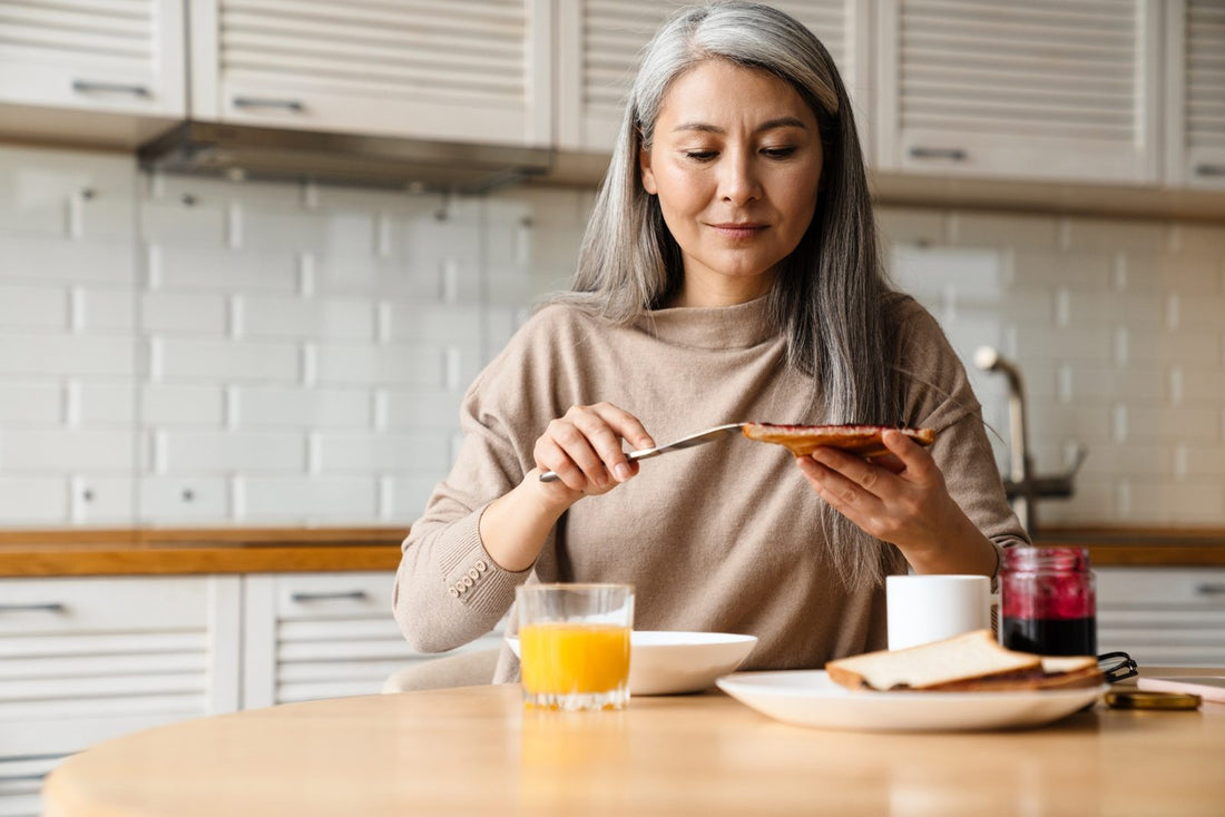 Grey-haired woman spreading jam on toast at breakfast, accompanying advice on coeliac disease later in life.