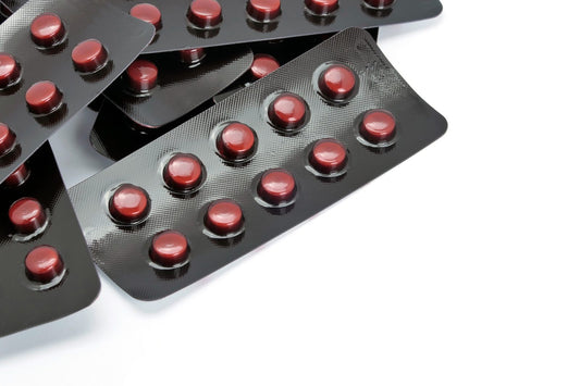 Close-up of red tablets in overlapping black blister packs on a white surface.