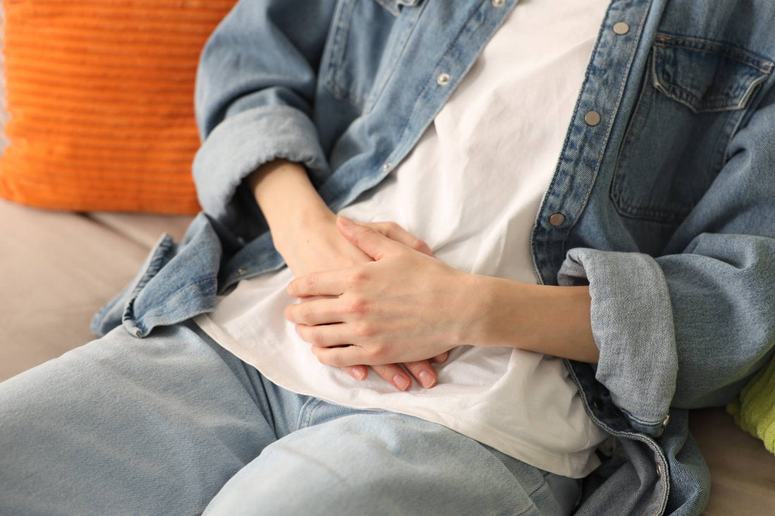 1. Person Sitting on a Sofa Holding Their Abdomen in Discomfort