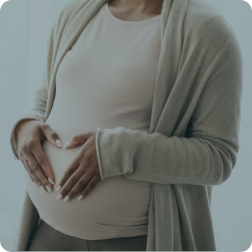 Pregnant person wearing a beige cardigan and shirt, holding their belly.